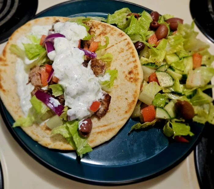 Marley Spoon pulled pork souvlaki on a flatbread with tzatziki, lettuce and red onion, next to a Greek salad with olives
