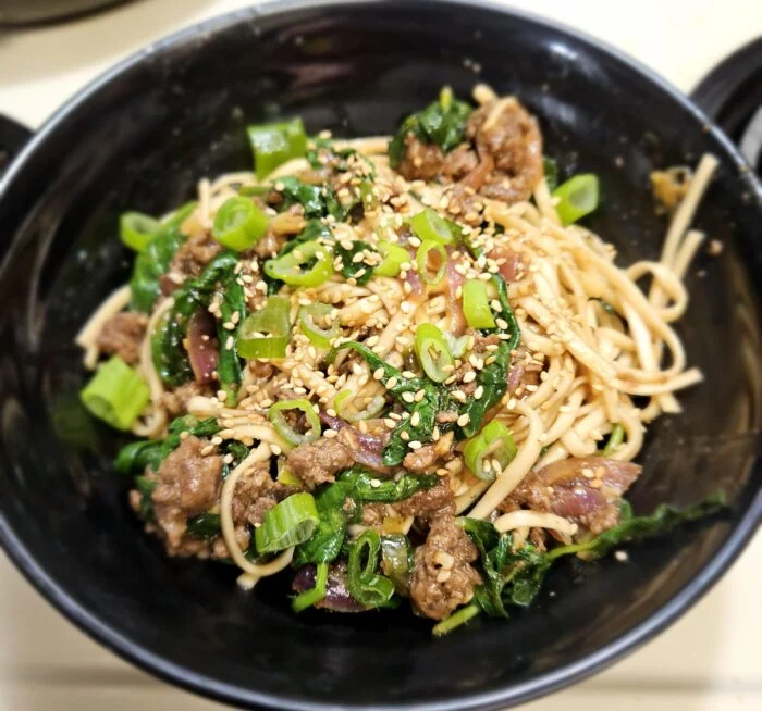 Marley Spoon sesame beef stir fry with noodles, spinach and scallions topped with sesame seeds in a black bowl