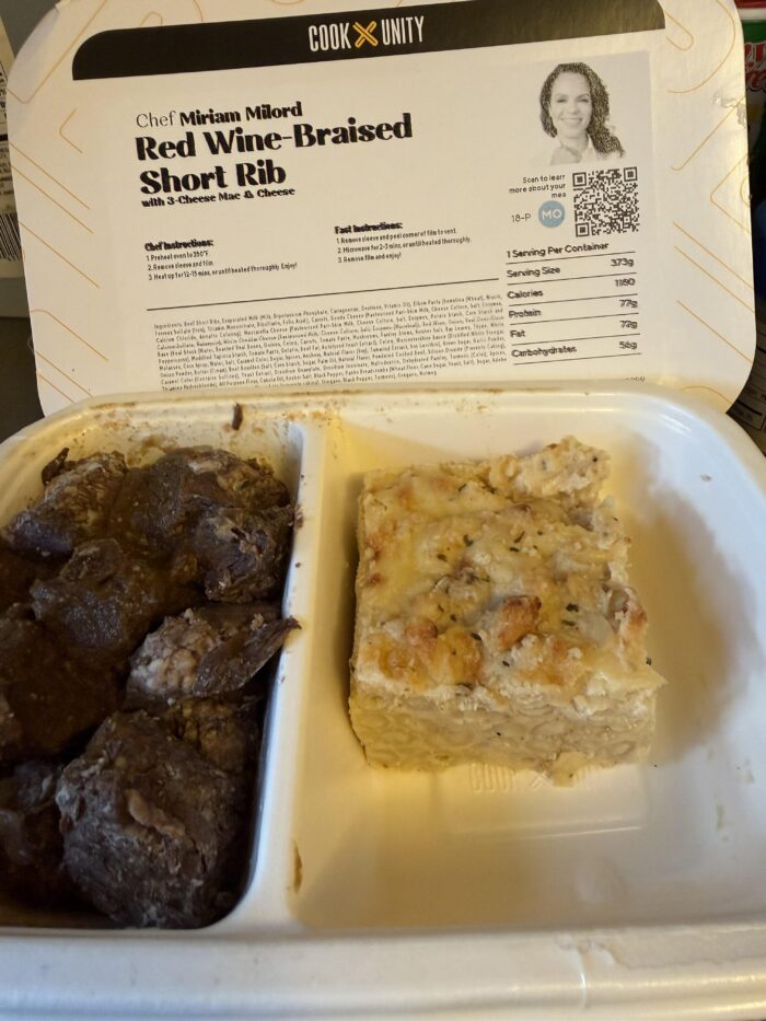 CookUnity red wine braised short rib in a dark sauce beside a square of baked three cheese mac and cheese, meal label open behind the tray