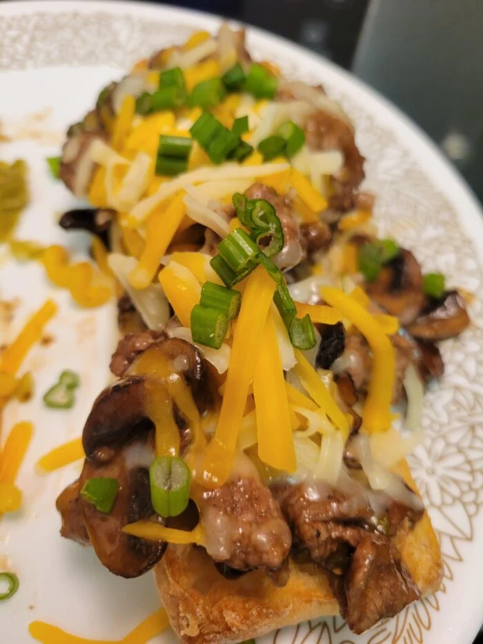 Blue Apron beef and mushroom baguette topped with melted shredded cheese and sliced scallions on a white plate