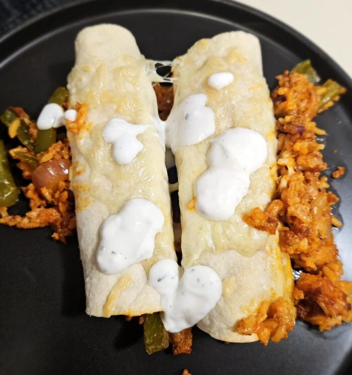 Blue Apron cheesy pork chorizo enchiladas topped with crema, with poblano peppers and chorizo rice on a black plate
