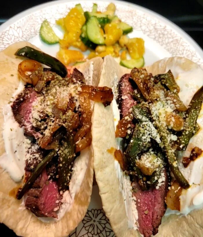 Blue Apron chipotle steak tacos with peppers, onions and sour cream, with orange and cucumber salad on a plate