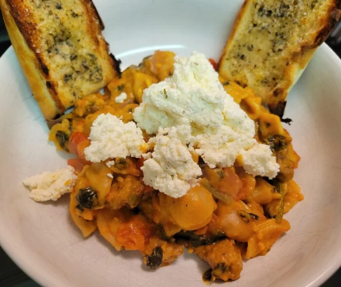 Blue Apron creamy tomato and sausage pasta with spinach and dollops of ricotta in a white bowl with two garlic bread slices