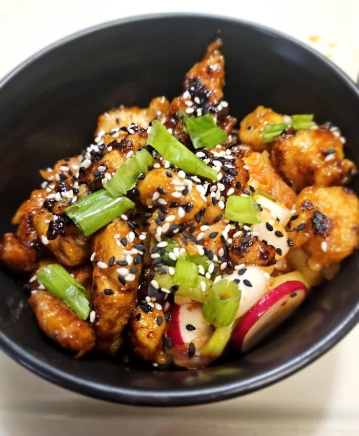Blue Apron crispy Korean style chicken with black and white sesame seeds, scallions and sliced radish in a black bowl