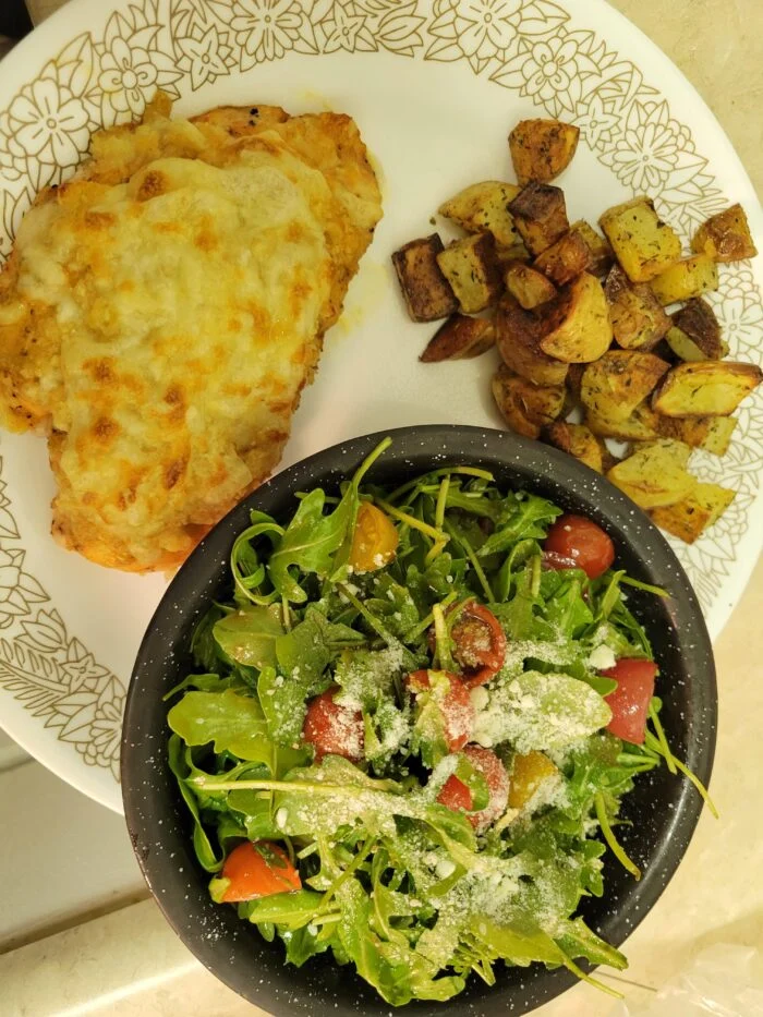 Blue Apron fontina panko crusted chicken with roasted potatoes and an arugula tomato salad with parmesan in a bowl
