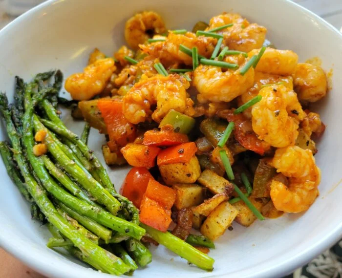 Blue Apron garlic shrimp with Spanish style potatoes, peppers, chives and roasted asparagus in a white bowl
