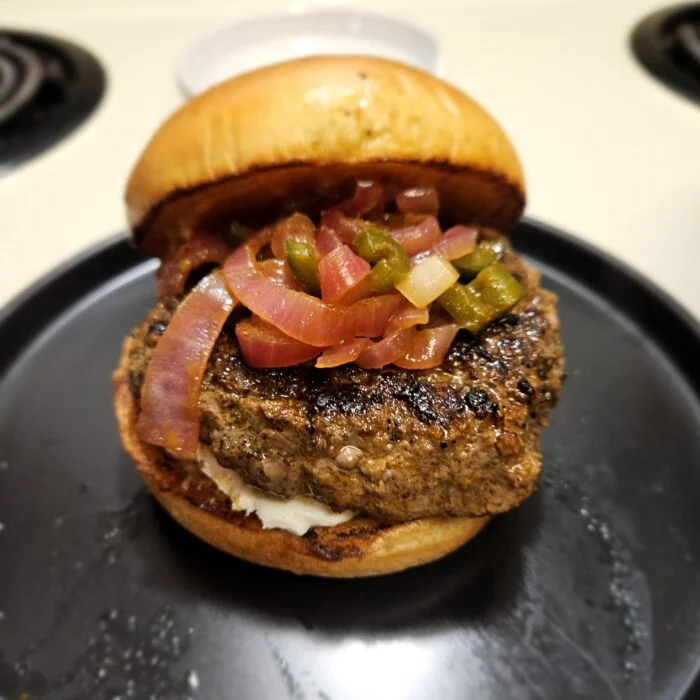 Blue Apron goat cheese burger with marinated jalapenos and pickled red onion on a toasted bun on a black plate