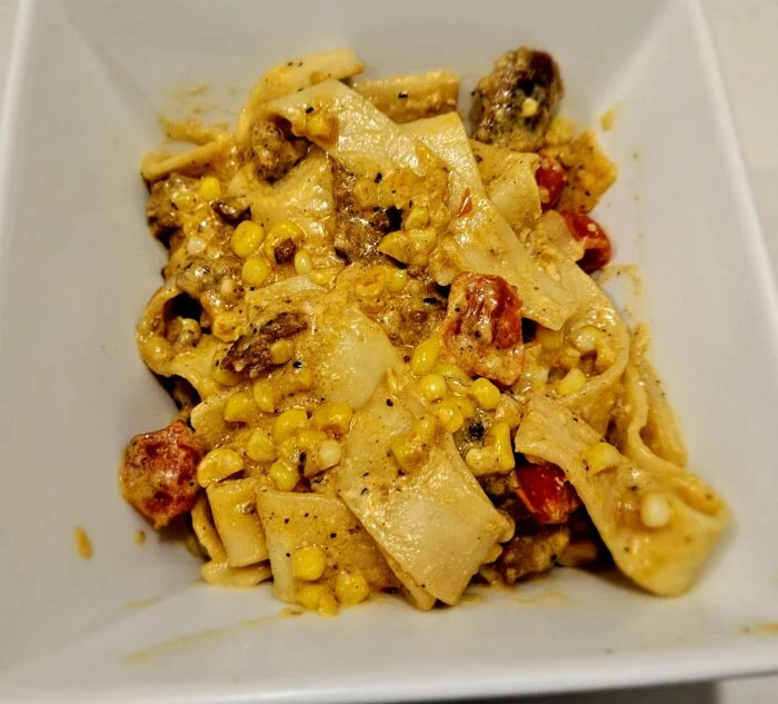 Blue Apron hand cut pappardelle with corn, roasted tomatoes and crumbled meat in a creamy sauce in a white square bowl