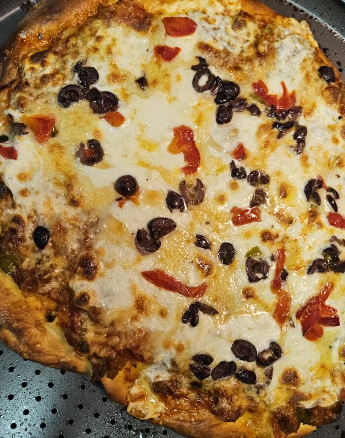 Blue Apron olive and fontina cheese pizza with black olives and red peppers on a perforated pizza pan