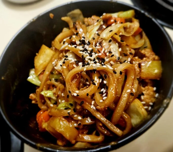 Blue Apron one pan pork and udon with ground pork, cabbage, carrots, bok choy and sesame seeds in a black bowl