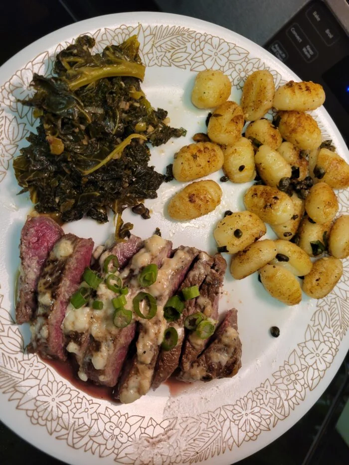 Blue Apron sliced seared steak with garlic aioli and scallions, crispy gnocchi with capers and sautéed kale on a plate
