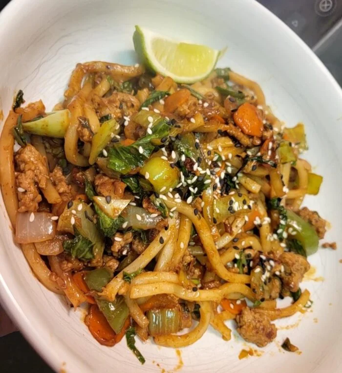 Blue Apron pork and udon noodles with bok choy, carrots, onion, sesame seeds and a lime wedge in a white bowl