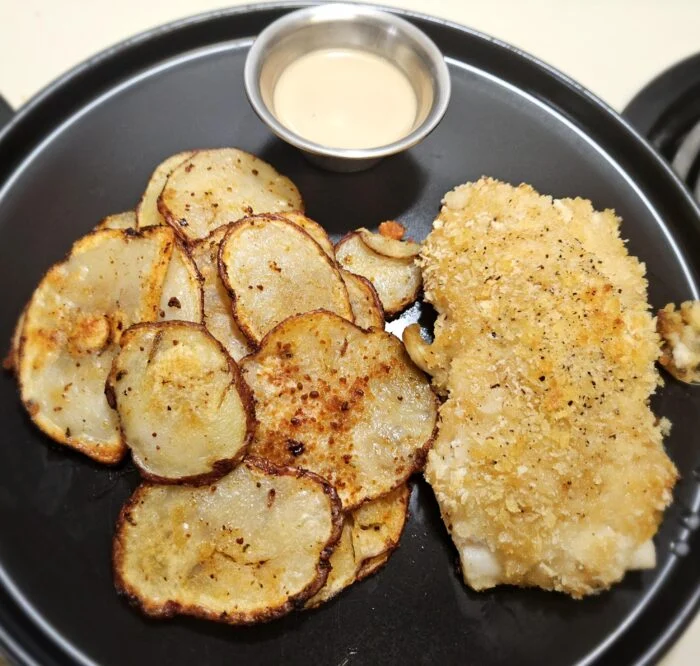 Blue Apron miso butter cod with a crumb crust, sliced roasted potatoes and a cup of ponzu mayo on a black plate