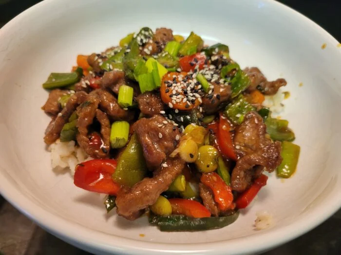 Blue Apron spicy glazed snap peas with beef, red peppers, scallions and sesame seeds over rice in a white bowl