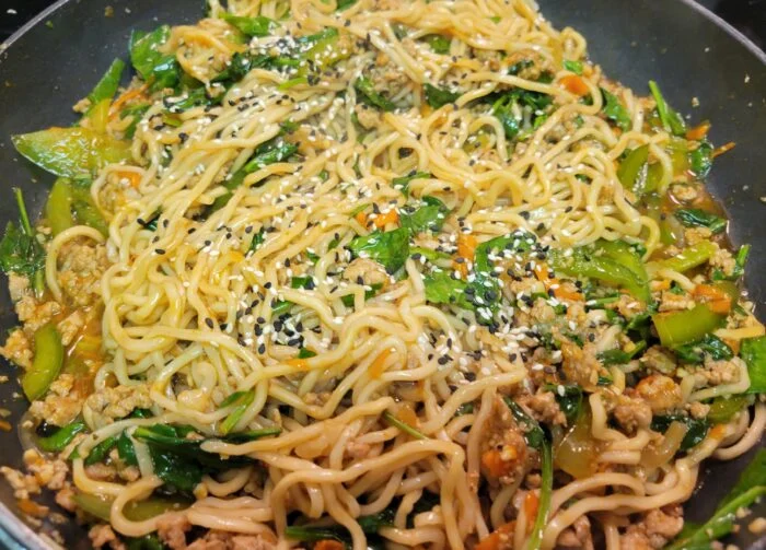 Blue Apron spicy pork lo mein with ground pork, spinach, carrots, green vegetables and sesame seeds in a skillet