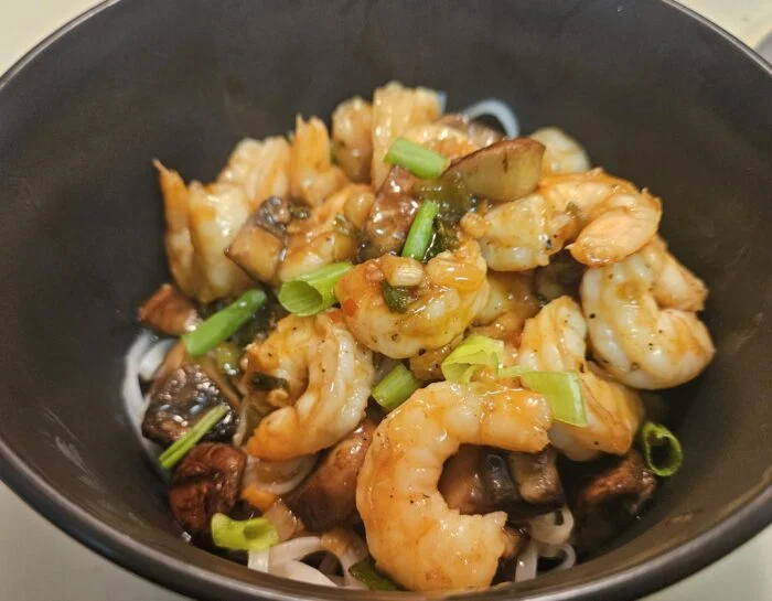 Blue Apron sweet chili shrimp with mushrooms and scallions over thin noodles in a black bowl