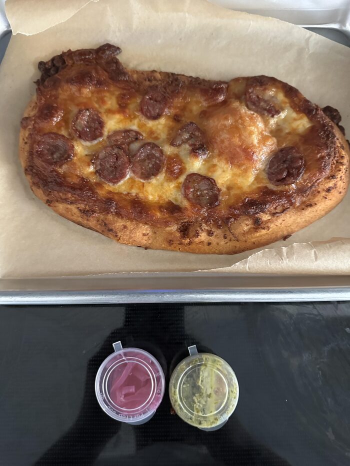 CookUnity chorizo provoleta pizza with browned melted cheese on parchment on a baking sheet, two sauce cups in front