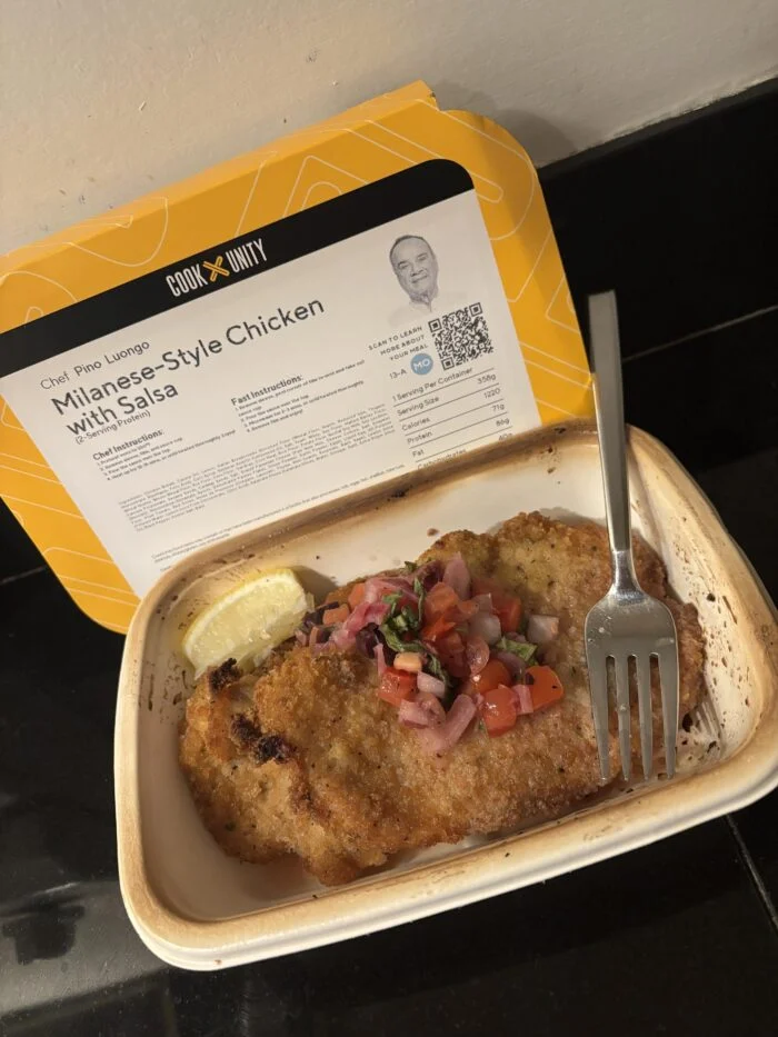 CookUnity Milanese style chicken with tomato and onion salsa and a lemon wedge in the tray, chef label open behind it