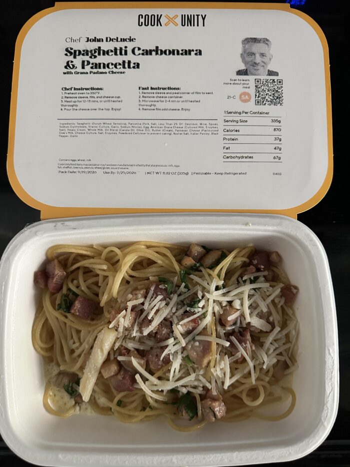 CookUnity spaghetti carbonara with pancetta and shaved cheese in the tray, chef label open behind it