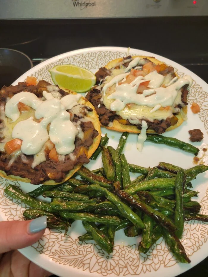 EveryPlate black bean and pepper jack tostadas with lime crema and pico de gallo, roasted green beans and lime on a plate
