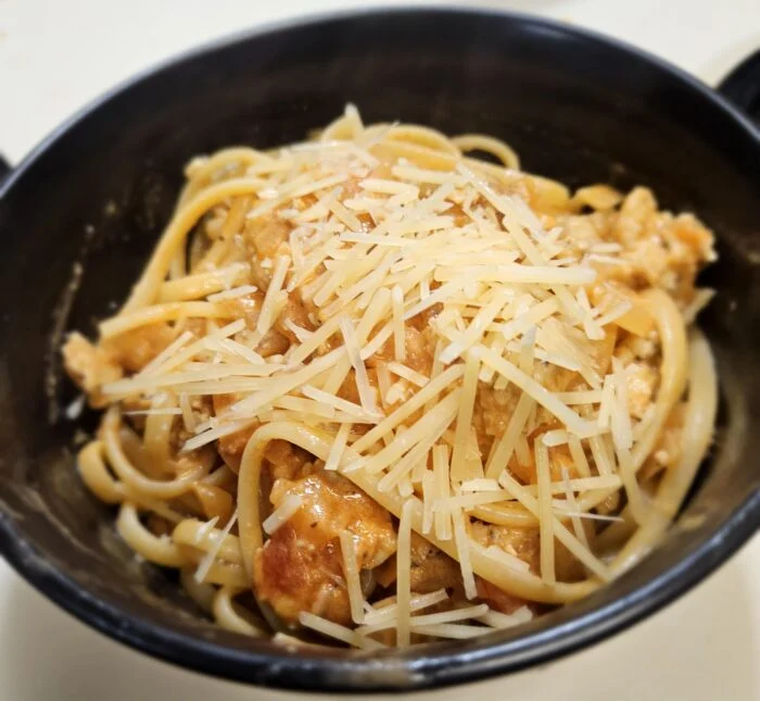 EveryPlate chicken sausage and roasted tomato linguine topped with shaved Parmesan in a black bowl