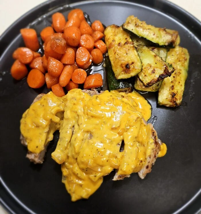 EveryPlate honey dijon pork chop with creamy sauce, glazed carrots and roasted zucchini wedges on a black plate