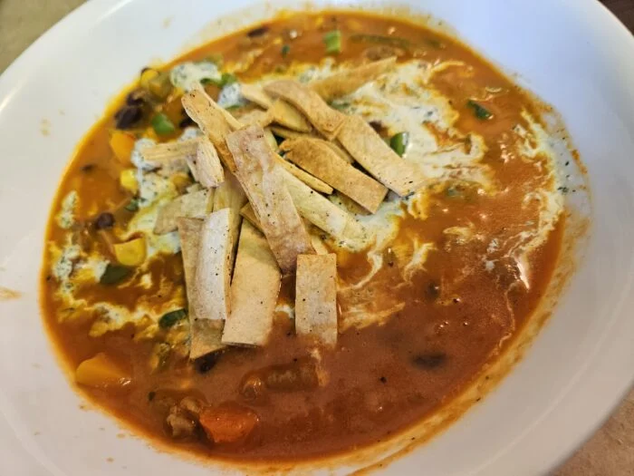 Green Chef butternut squash chili with black beans, corn, tortilla strips and a crema swirl in a white bowl