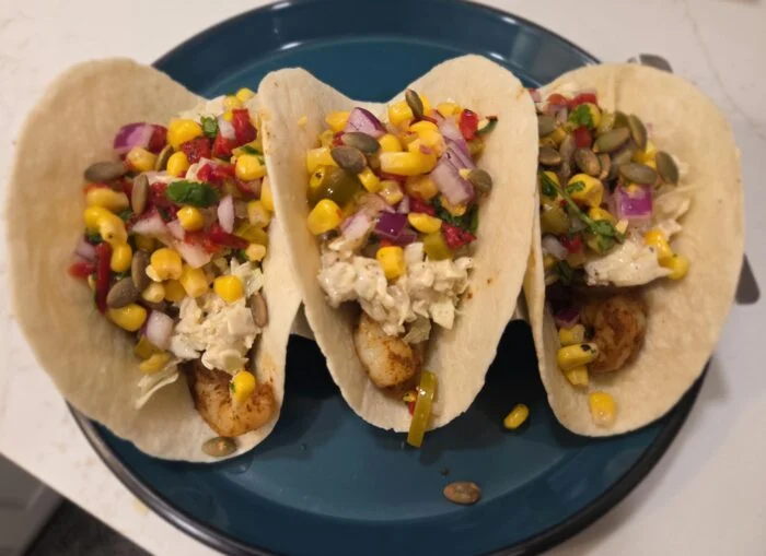 Green Chef Mexican spiced shrimp tacos with corn salsa, slaw and pepitas in flour tortillas on a teal plate