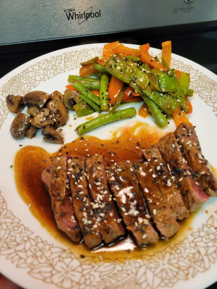 Green Chef Mongolian BBQ ranch steak sliced with sesame and sauce, snap peas, peppers and mushrooms on a plate