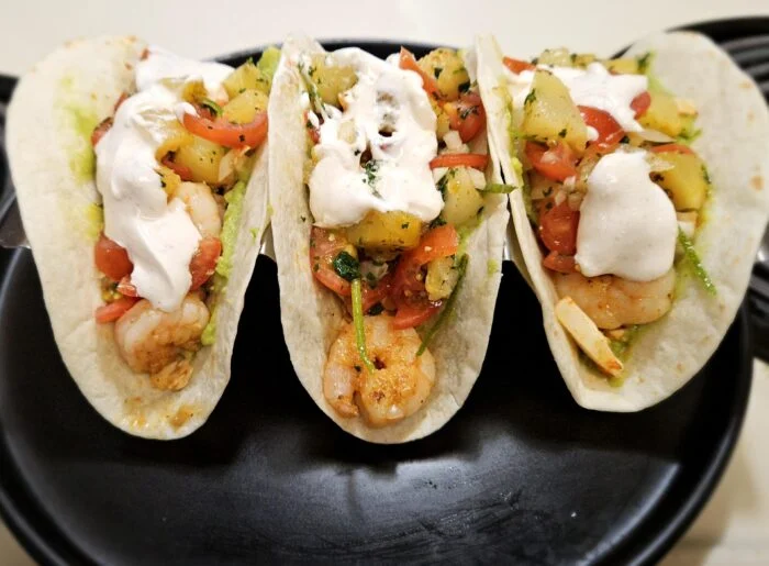 Green Chef shrimp tacos with pineapple salsa, tomato, crema and avocado in flour tortillas on a black plate