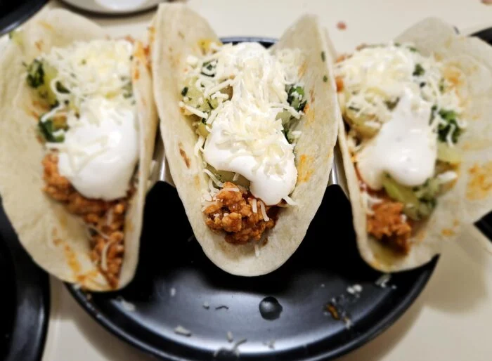 Green Chef spiced pork tacos with shredded cheese, sour cream and chopped green salsa in flour tortillas on a black plate