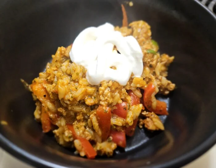 Green Chef spicy turkey and rice skillet with red peppers, topped with sour cream in a black bowl
