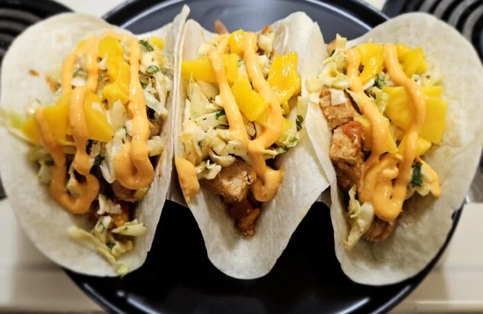 Green Chef Thai spiced chicken tacos with mango, slaw and a spicy mayo drizzle, three tacos on a black plate