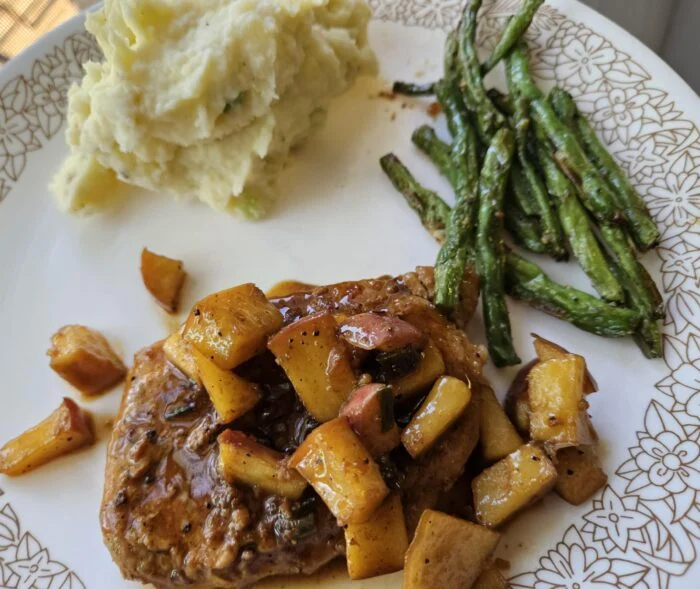 HelloFresh pork chop topped with apple pan sauce, scallion mashed potatoes and roasted green beans on a patterned plate