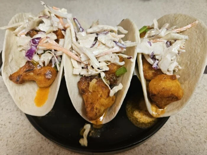 HelloFresh buffalo cauliflower tacos topped with creamy slaw on flour tortillas on a black plate