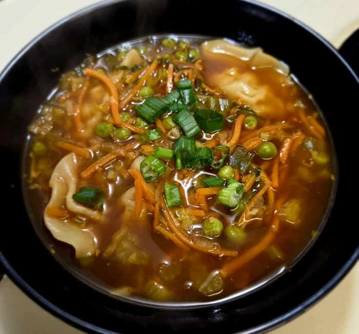 HelloFresh chicken gyoza in shoyu style broth with shredded carrots, peas and scallions in a black bowl