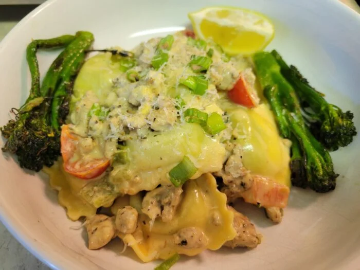 HelloFresh chicken sausage and spinach ricotta ravioli with tomatoes, scallions, roasted broccolini and lemon in a bowl
