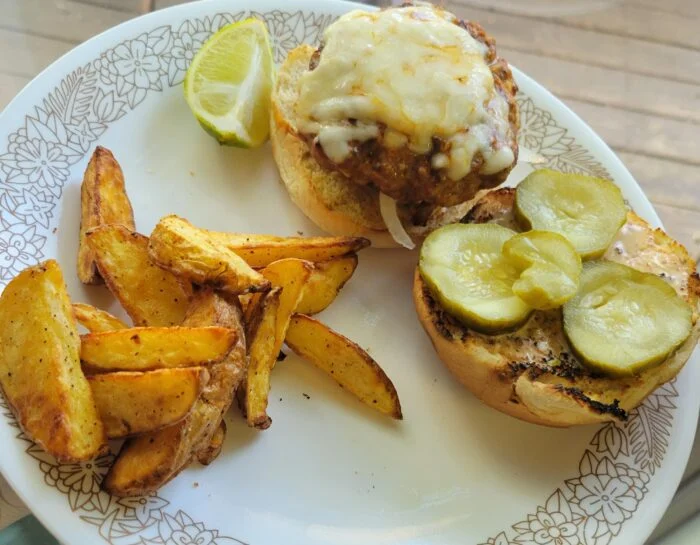 HelloFresh citrus mojo pork burger with melted cheese, pickles and a lime wedge beside potato wedges on a floral plate
