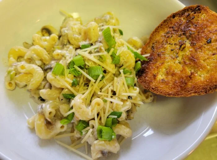HelloFresh creamy chicken sausage and mushroom cavatappi with scallions and grated cheese in a white bowl with garlic bread