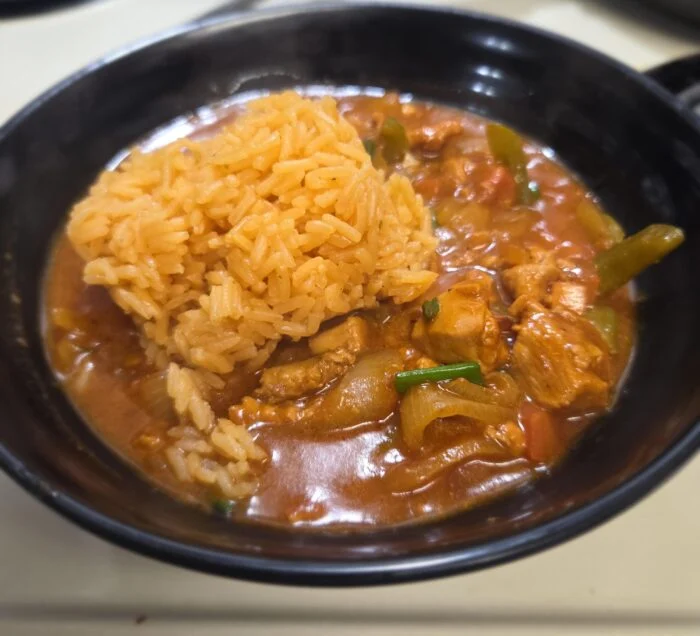 HelloFresh Dominican style pollo guisado, chicken stew with peppers and onions beside seasoned rice in a black bowl