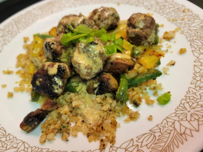 HelloFresh firecracker meatballs with creamy sauce over cauliflower rice with green beans, mushrooms and peppers on a plate