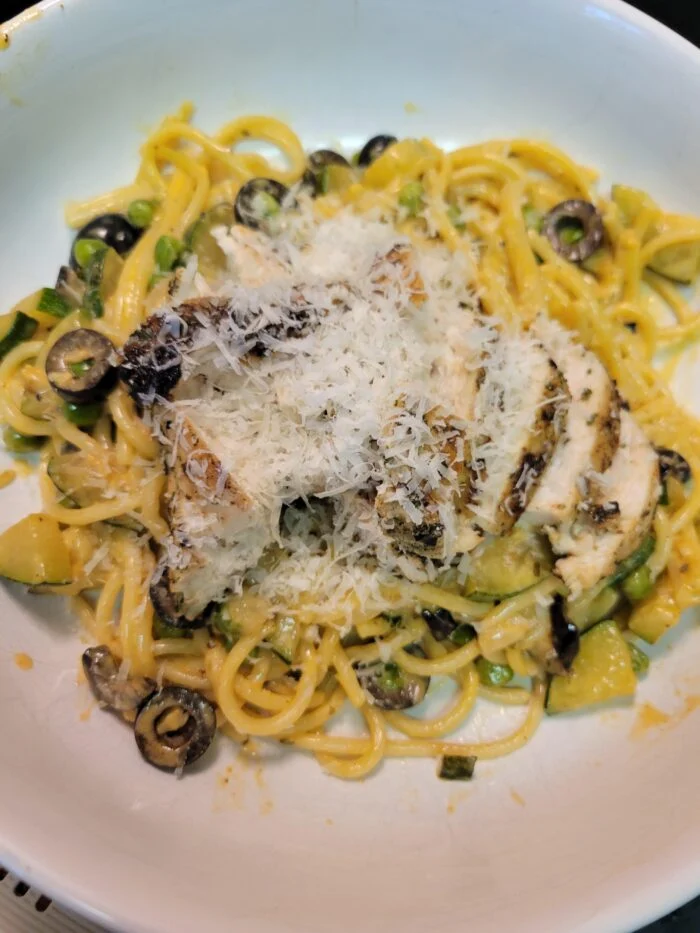 HelloFresh Italian chicken sliced over lemony spaghetti with zucchini, peas, black olives and grated parmesan in a bowl