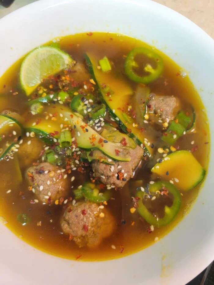 HelloFresh pho style beef meatball soup with zucchini noodles, jalapeno, lime, sesame and chili flakes in a white bowl