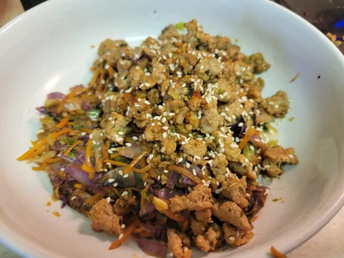 HelloFresh pork egg roll in a bowl with ground pork, shredded cabbage, carrots and sesame seeds in a white bowl
