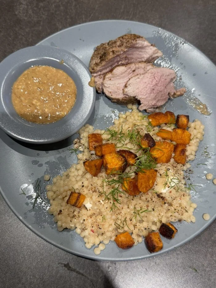 HelloFresh sliced pork filet with a dish of creamy garlic sauce, pearl couscous and roasted squash cubes on a grey plate