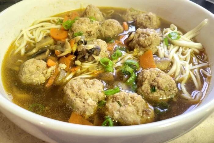 HelloFresh pork meatball and mushroom ramen with noodles, carrots and scallions in broth in a white bowl