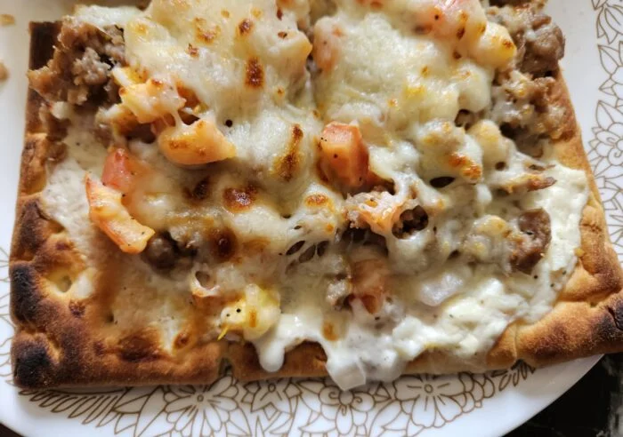HelloFresh pork sausage flatbread with melted mozzarella and chopped roma tomatoes on a patterned plate