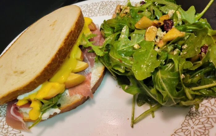 HelloFresh prosciutto, ricotta and apple sandwich with honey dijon sauce beside an arugula salad with cranberries and cheese