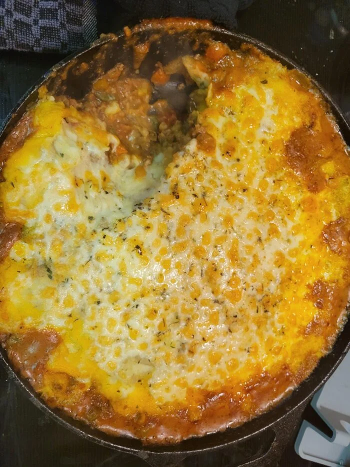 HelloFresh pub style shepherd's pie with a melted cheese topping in a cast iron skillet, one portion scooped out
