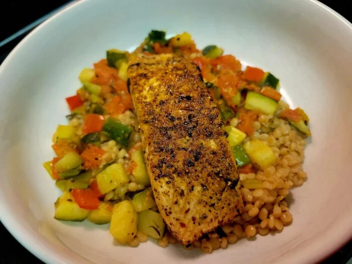HelloFresh salmon limone fillet over herbed pearl couscous with zucchini and tomato in a white bowl